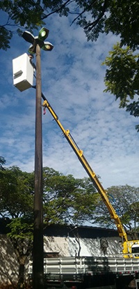 guindaste Rodomunk operando com cesto aéreo para elevar um eletricista até o topo de um poste (rede/iluminação), com árvores ao fundo e céu azul; foco na aplicação de eletrificação e manutenção de redes.