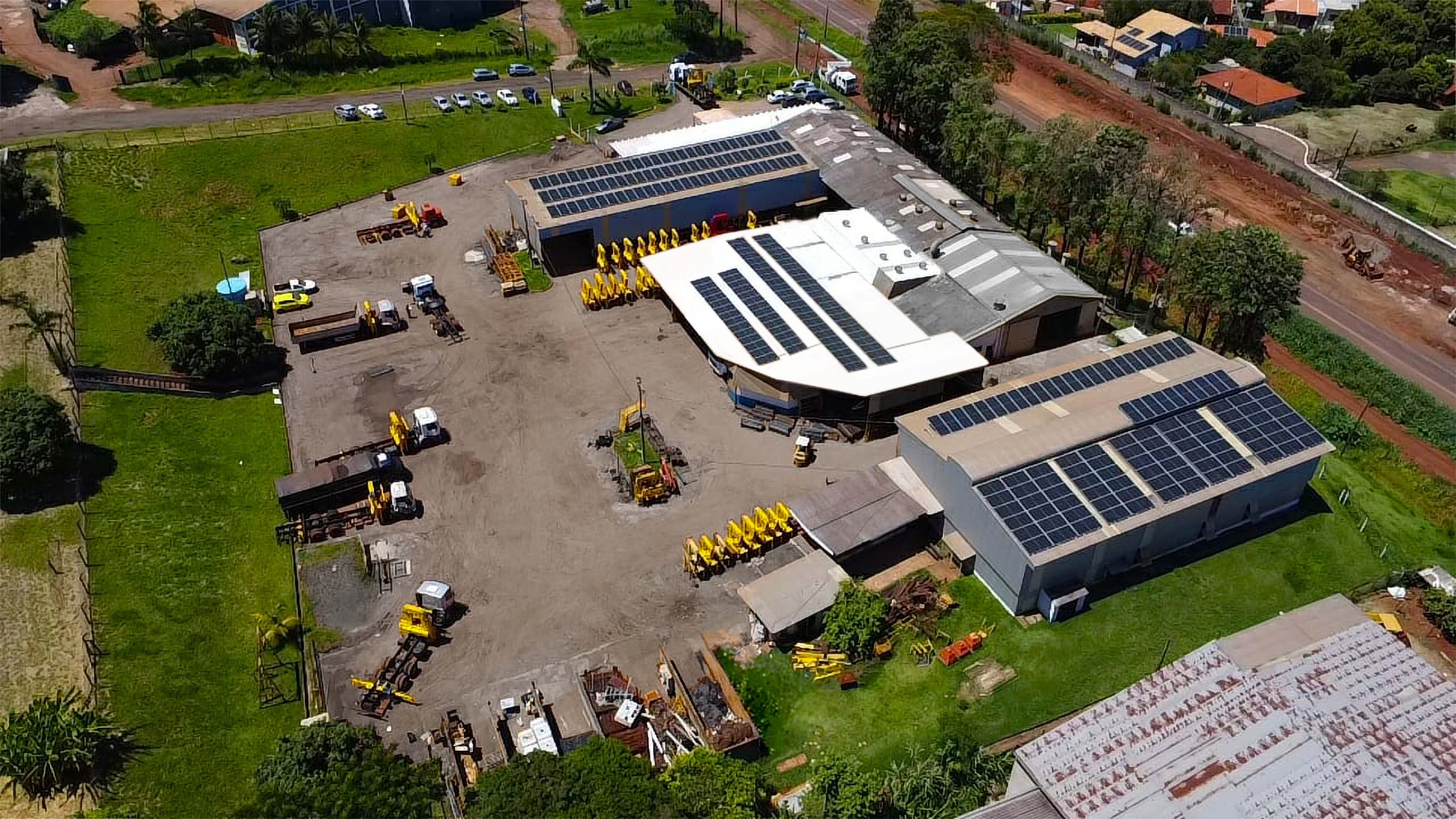 vista aérea do complexo industrial/pátio da Rodomunk, com galpões, área de montagem e estoque, caminhões e equipamentos estacionados; ao lado, estrada e áreas verdes ao redor do parque fabril.