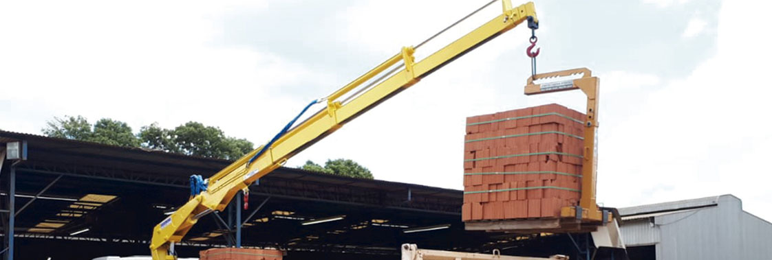 Guindaste veicular realizando carregamento de palete de tijolos em caminhão durante operação logística.