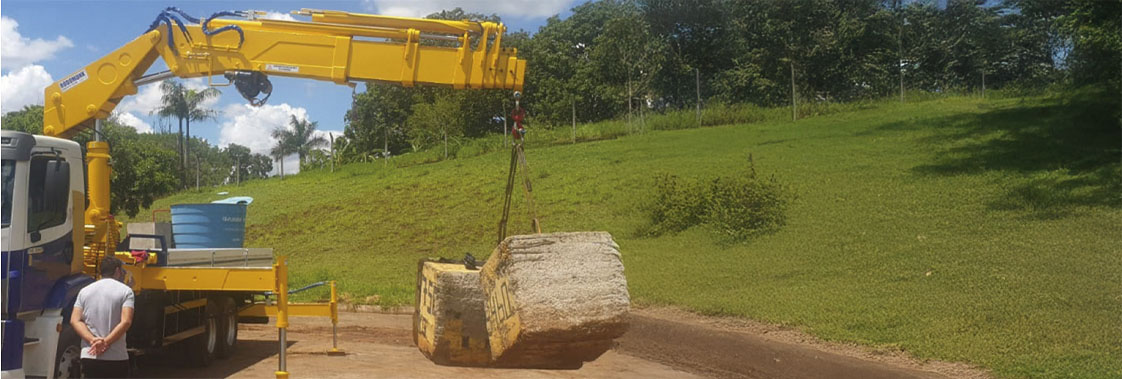 Guindaste veicular articulado em caminhão levantando carga durante operação de movimentação com braço hidráulico.