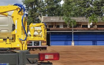 Guindaste veicular articulado instalado em caminhão, mostrando estrutura montada no chassi para operações de movimentação de carga.
