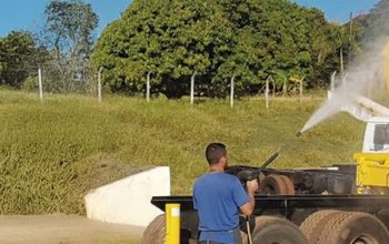Operador lavando guindaste veicular com jato de pressão durante limpeza e manutenção do equipamento.
