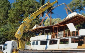 Guindaste veicular içando estrutura de telhado com cintas de amarração durante operação de movimentação de carga.