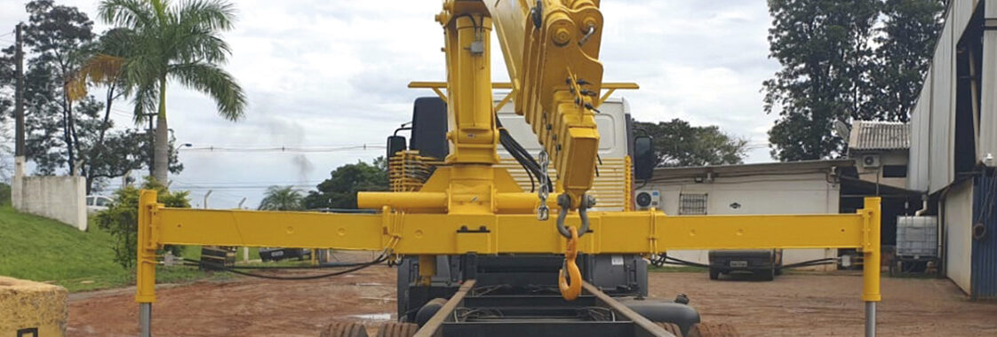 Guindaste veicular com patolas totalmente abertas e apoiadas no solo, demonstrando o patolamento correto para ampliar a base de sustentação e garantir estabilidade durante a operação de içamento.